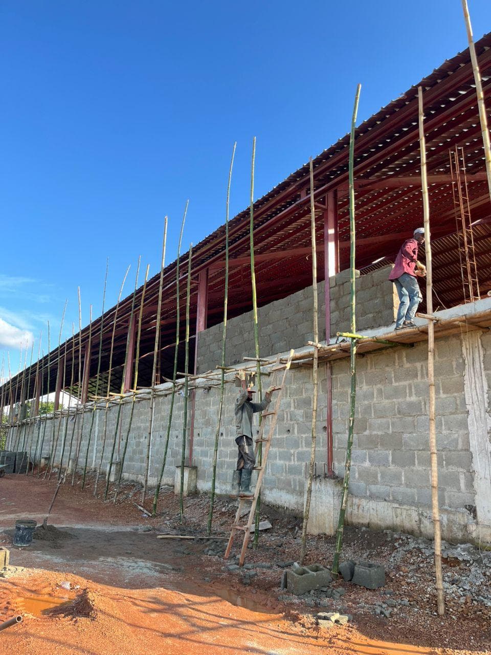 Workers on bamboo scaffolding building a blockwork wall under a steel roof