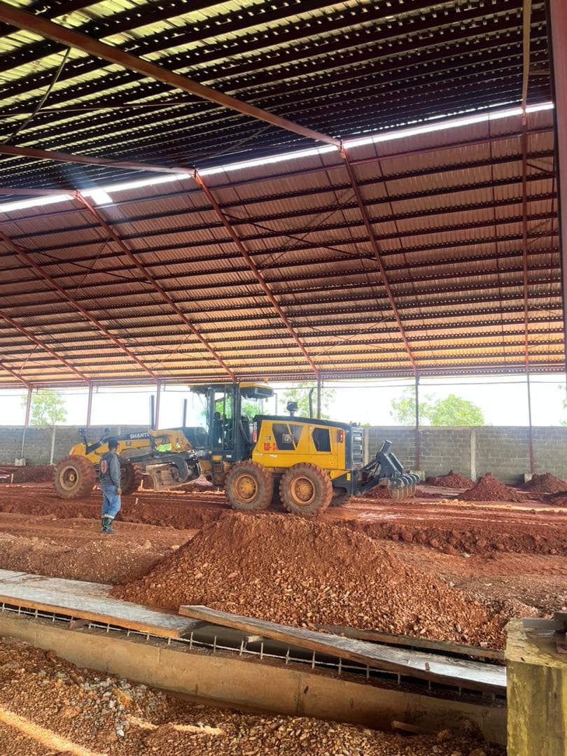 Motor grader levelling the ground inside a newly roofed steel-frame building