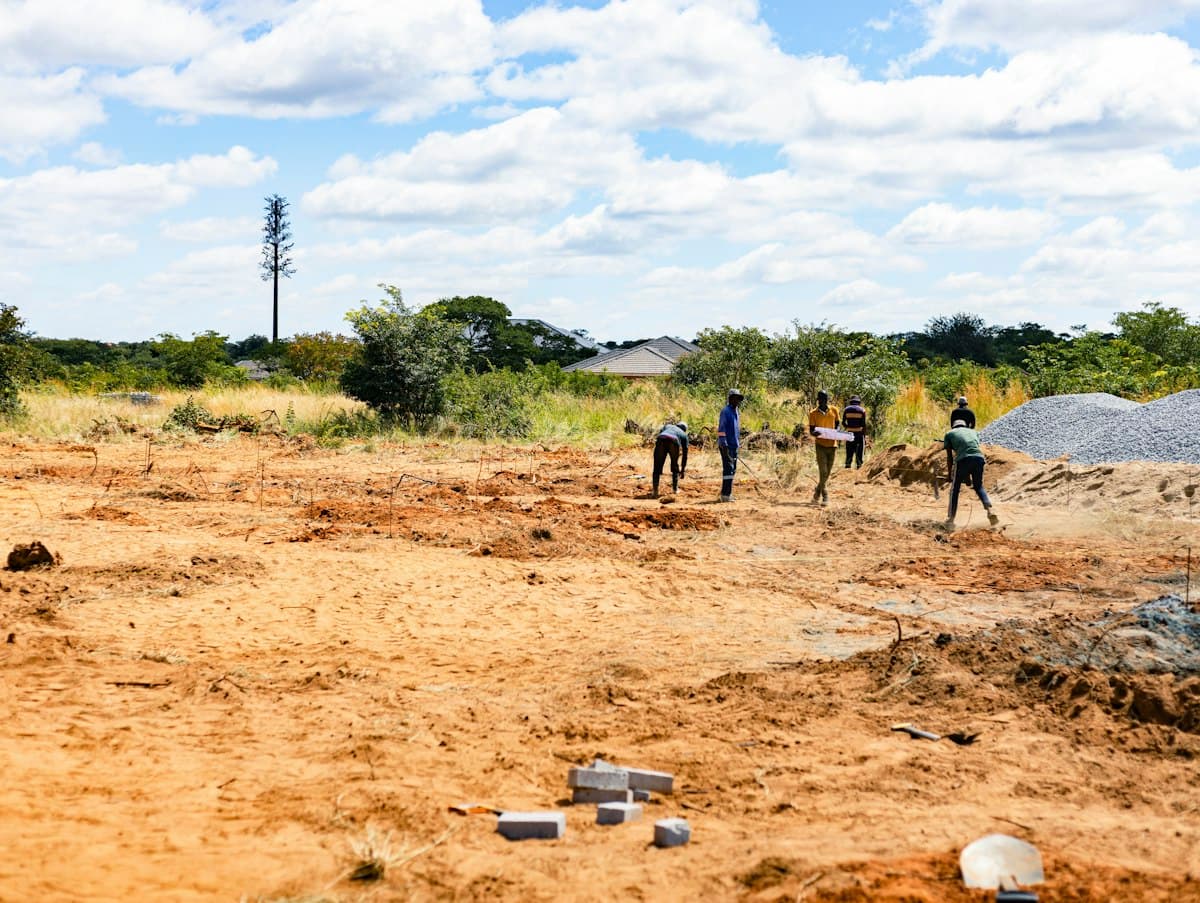 Cleared plot of land with red soil and workers marking out the site